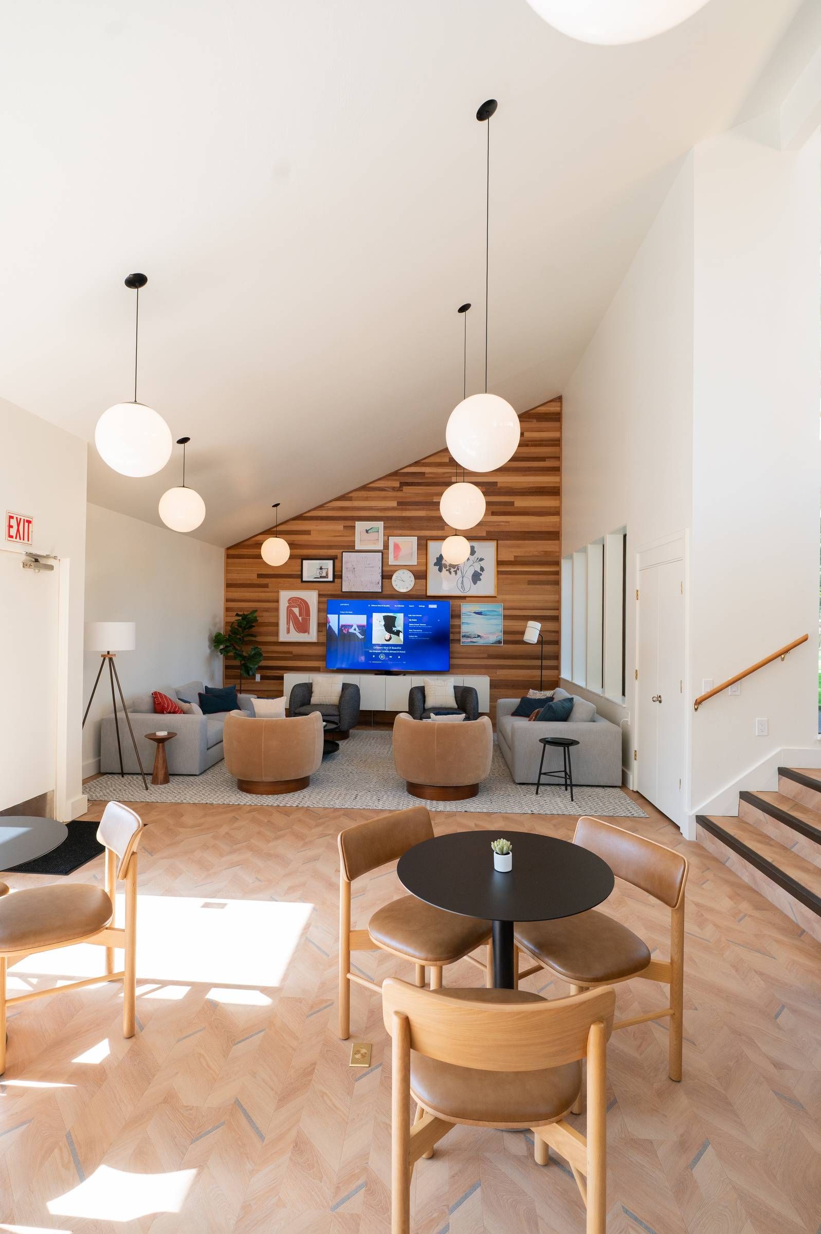 Northgreen Apartments Modern lounge with wooden accents, round tables, chairs, sofas, wall art, and hanging globe lights.