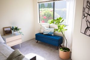 Northgreen Apartments Bright bedroom with a blue bench, potted plants, and large window showing a garden outside.