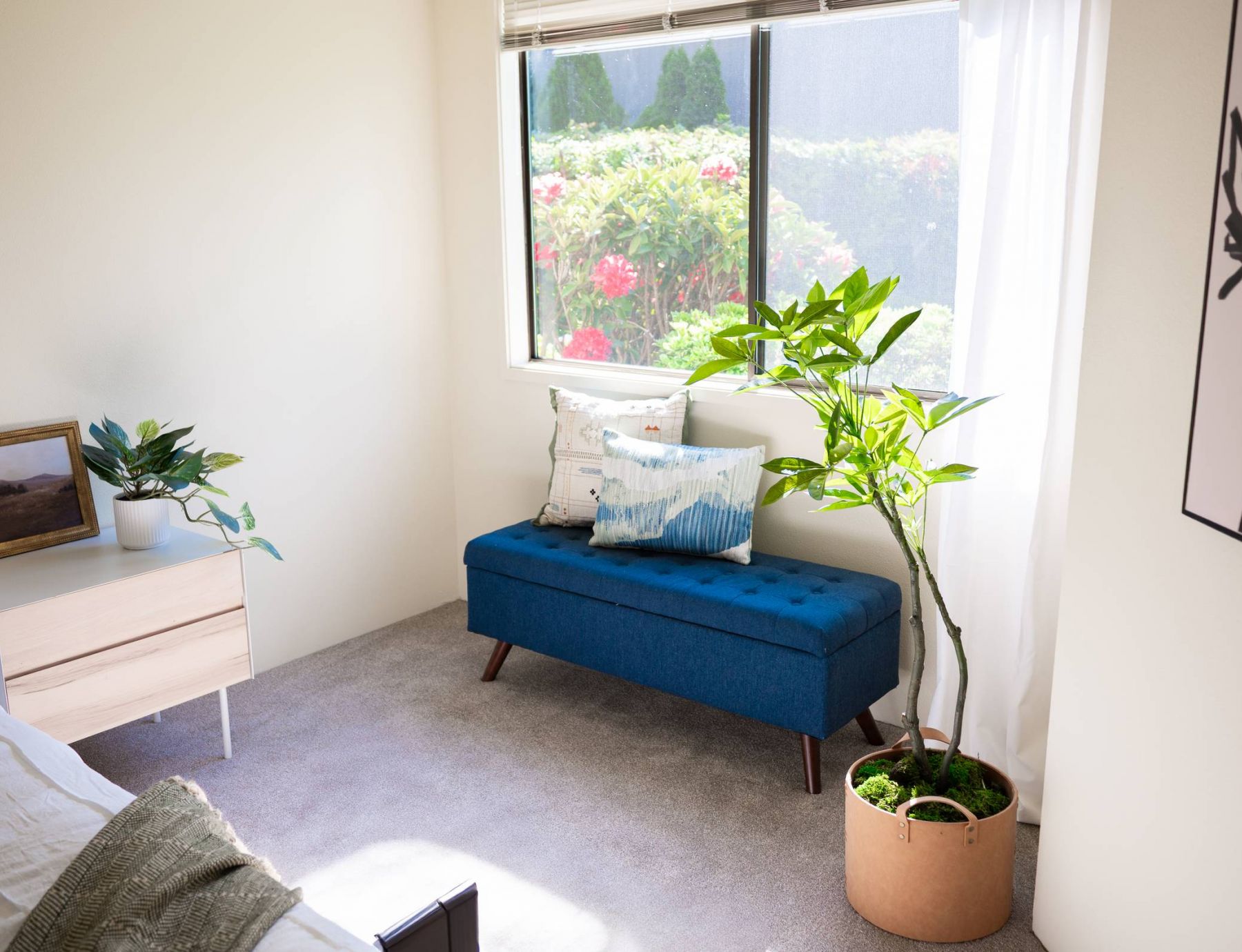 Northgreen Apartments Bright bedroom with a blue bench, potted plants, and large window showing a garden outside.