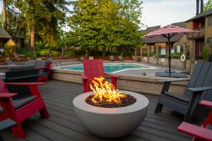 Northgreen Apartments Red and gray chairs surround a round fire pit near a pool with trees and an umbrella in the background.
