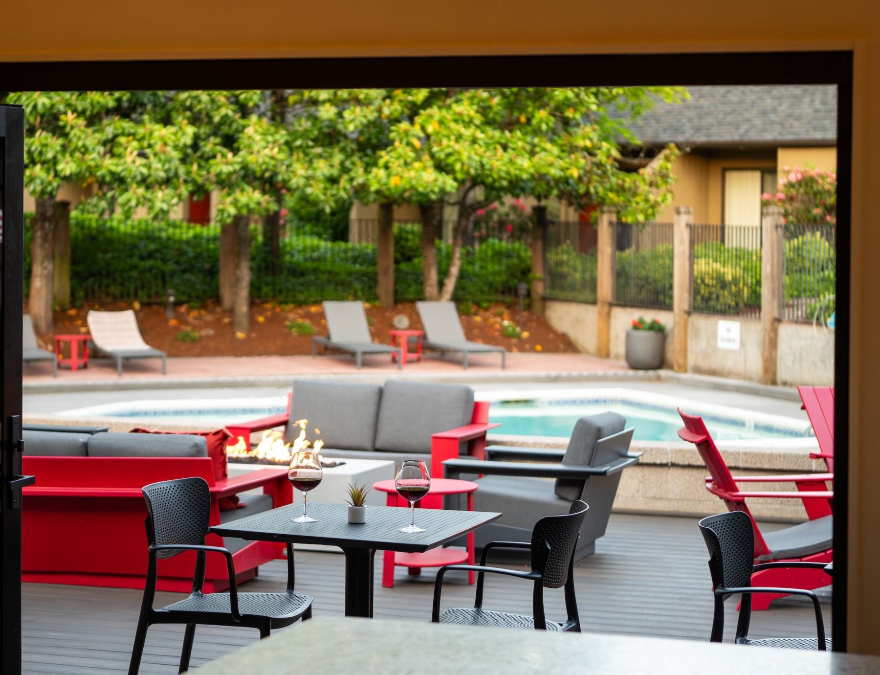 Northgreen Apartments Outdoor patio with red chairs, fire pit, wine glasses on tables, and a pool surrounded by lounge chairs.