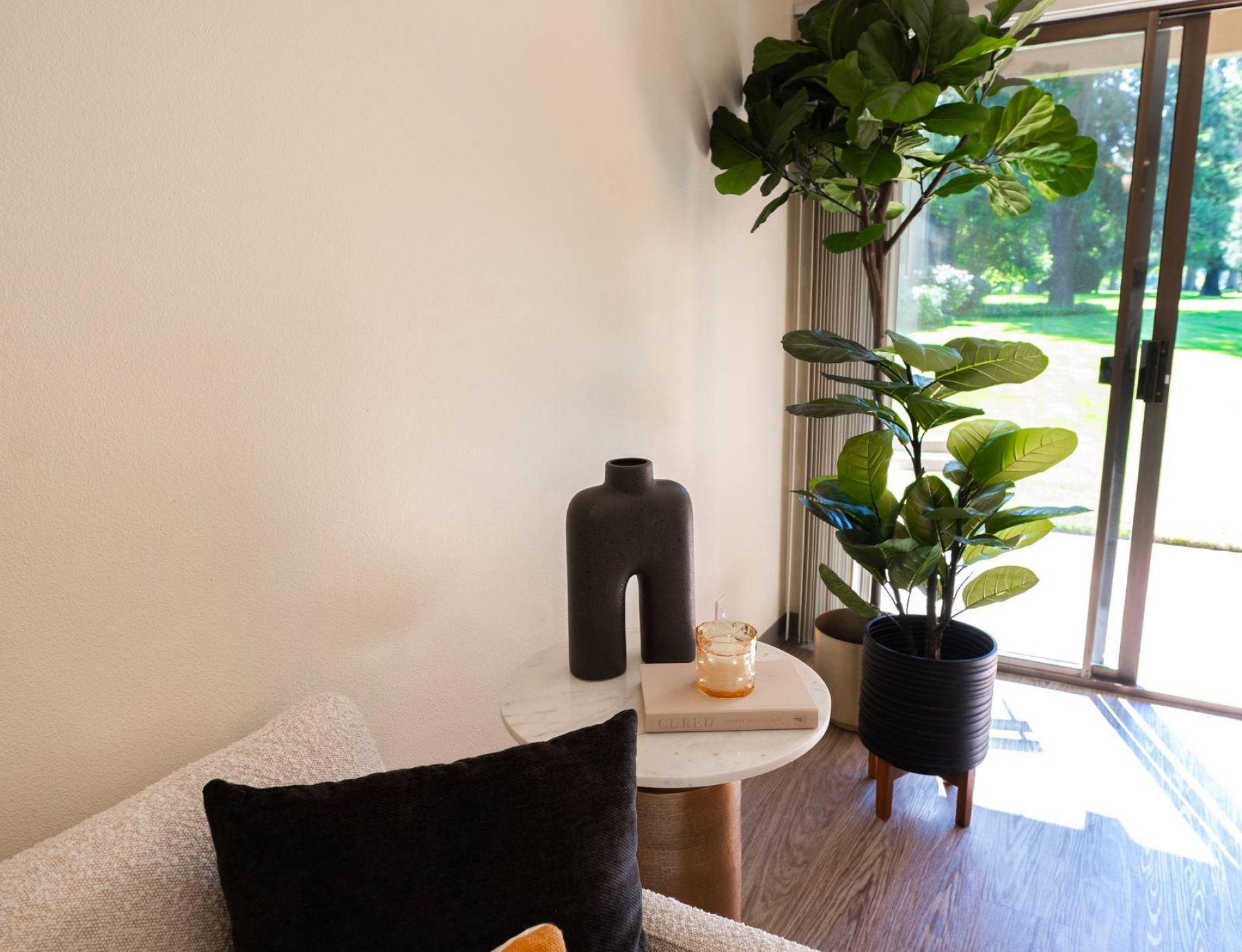 Northgreen Apartments Modern living room corner with a cozy armchair, side table, plant, and sliding glass door to a green lawn.
