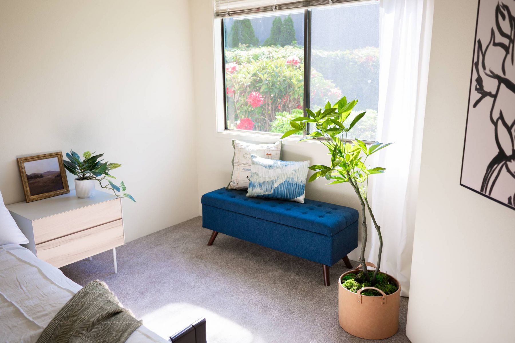 Northgreen Apartments Bright bedroom with a blue bench, potted plants, and large window showing a garden outside.