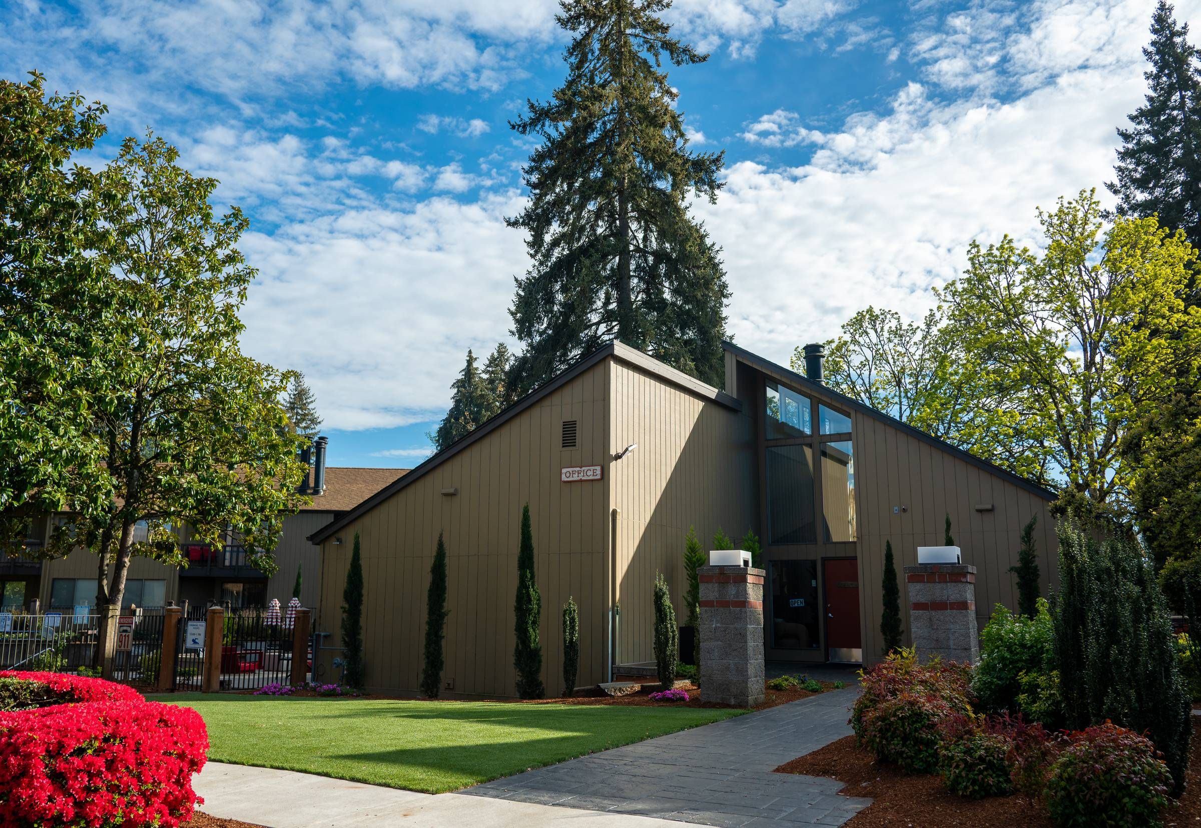 Northgreen Apartments Modern building with large windows, surrounded by trees, shrubs, and a well-kept lawn under a blue sky.