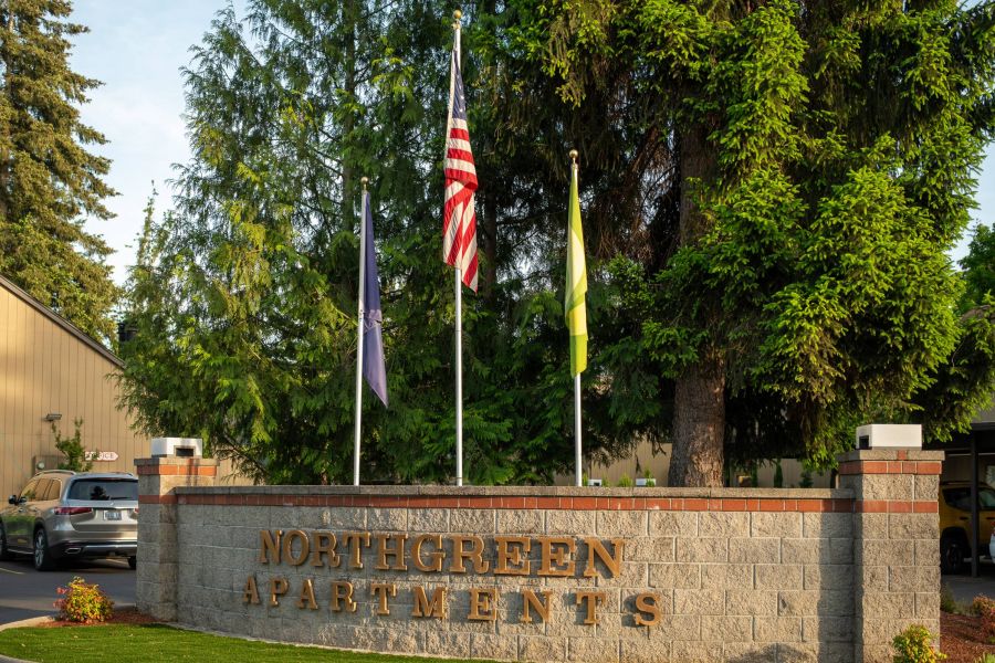 Northgreen Apartments Brick sign reading "NORTHGREEN APARTMENTS" with three flags and trees in the background.