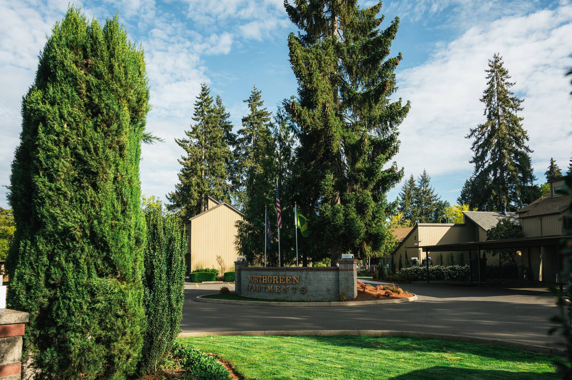 Northgreen Apartments Entrance to Sherreen Apartments with tall trees, green lawn, and a clear, partly cloudy sky.