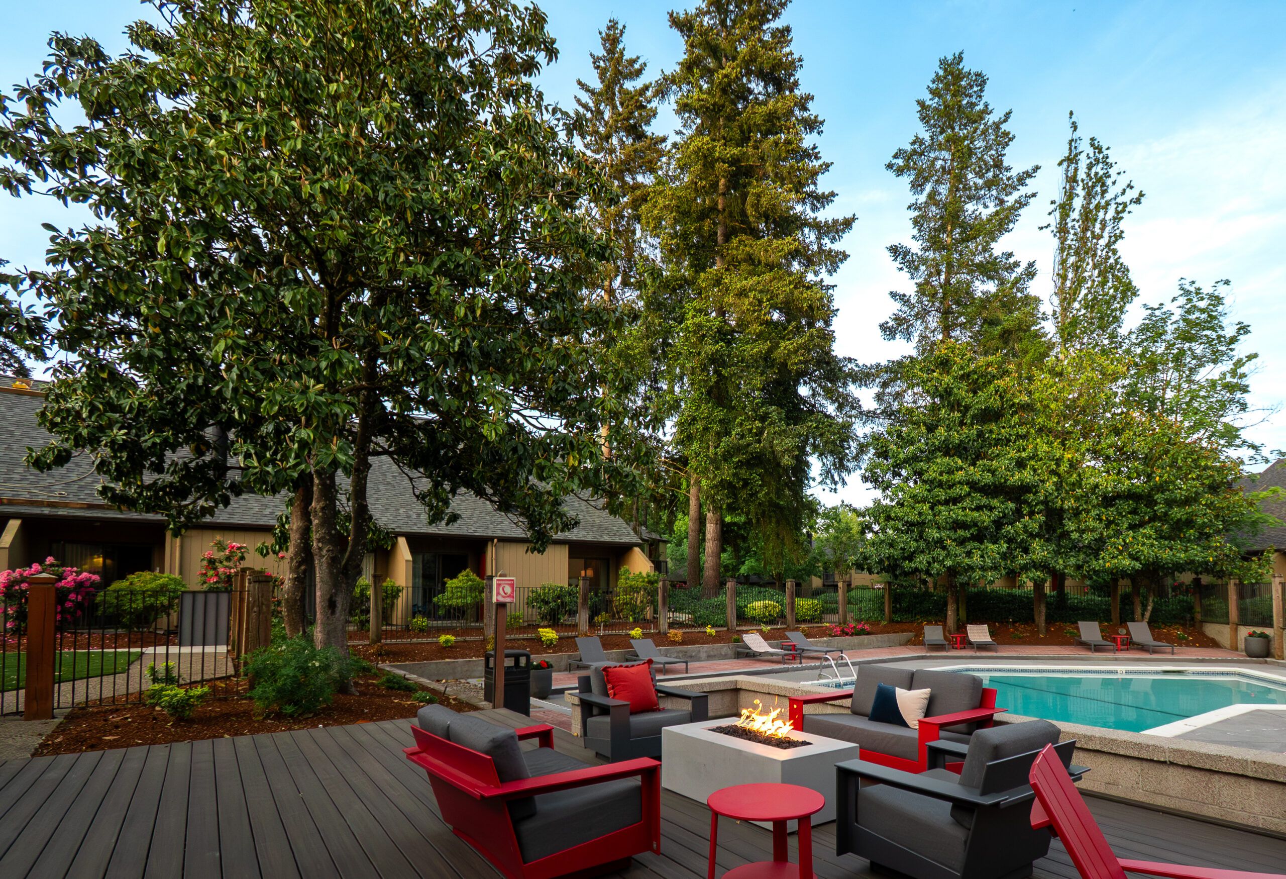 Northgreen Apartments Modern patio with red and black chairs around a fire pit, next to a pool and tall trees in the background.