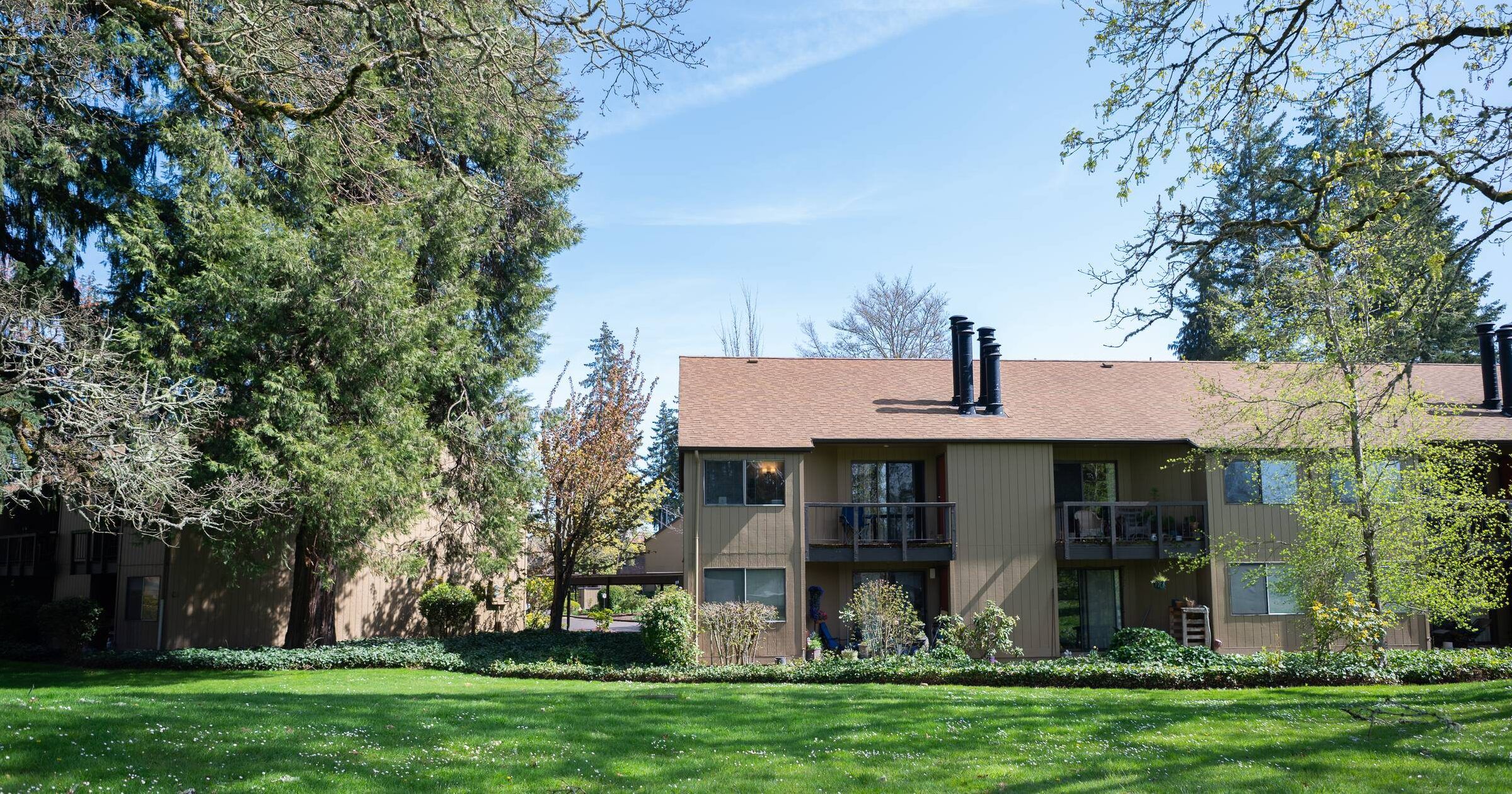 Northgreen Apartments Apartment building with balconies surrounded by green grass, trees, and a sunny blue sky.