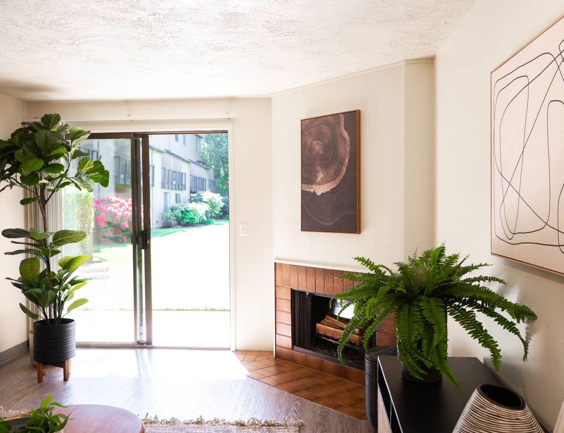 Northgreen Apartments Bright living room with plants, a fireplace, modern art, and a sliding glass door leading to a green yard.